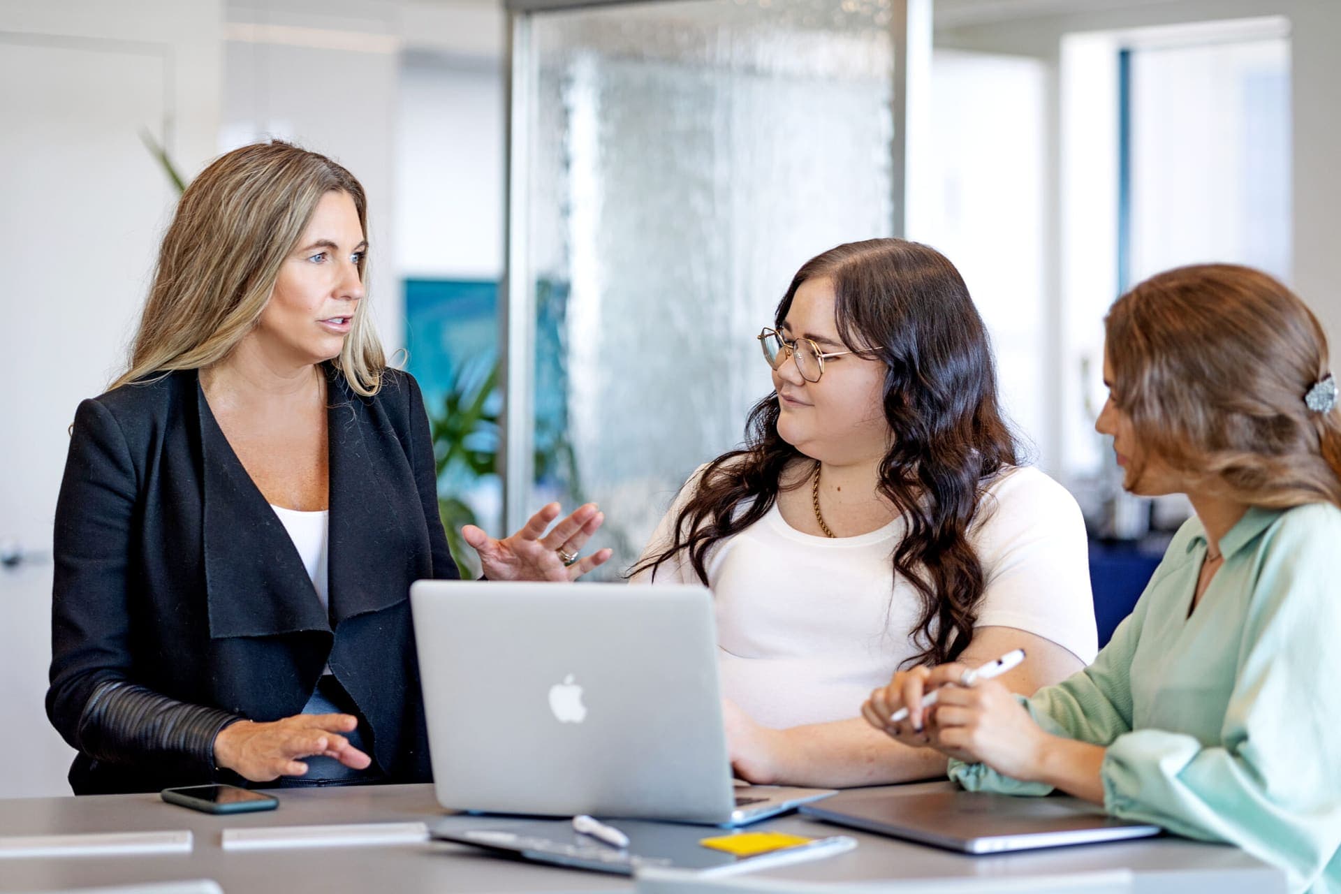 A Level Up facilitator coaching two leaders around a laptop at a conference table.